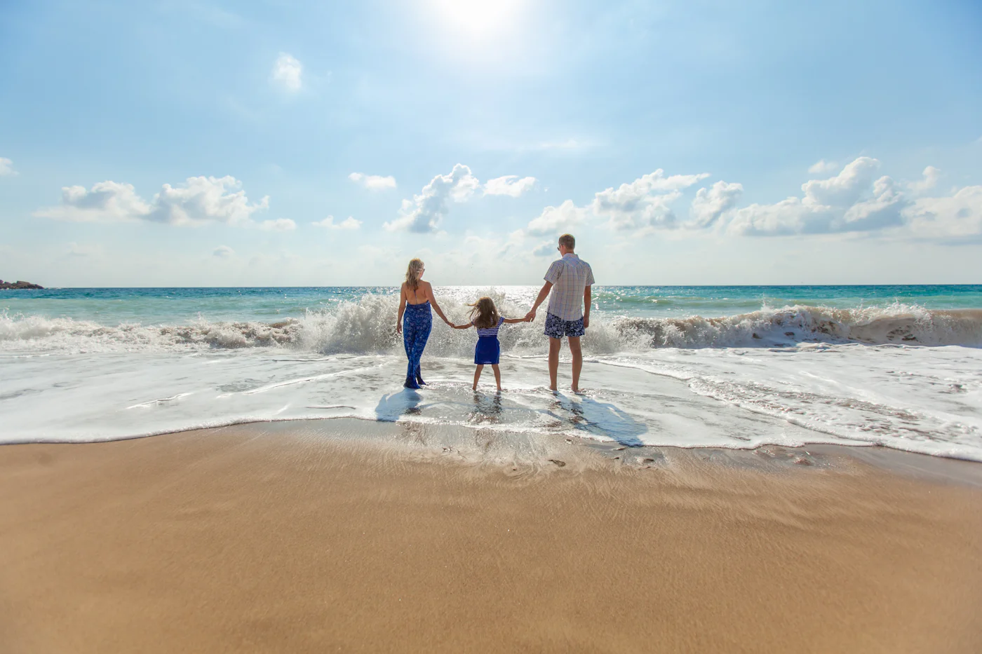 A family holding hands, walking along the shoreline at the water's edge