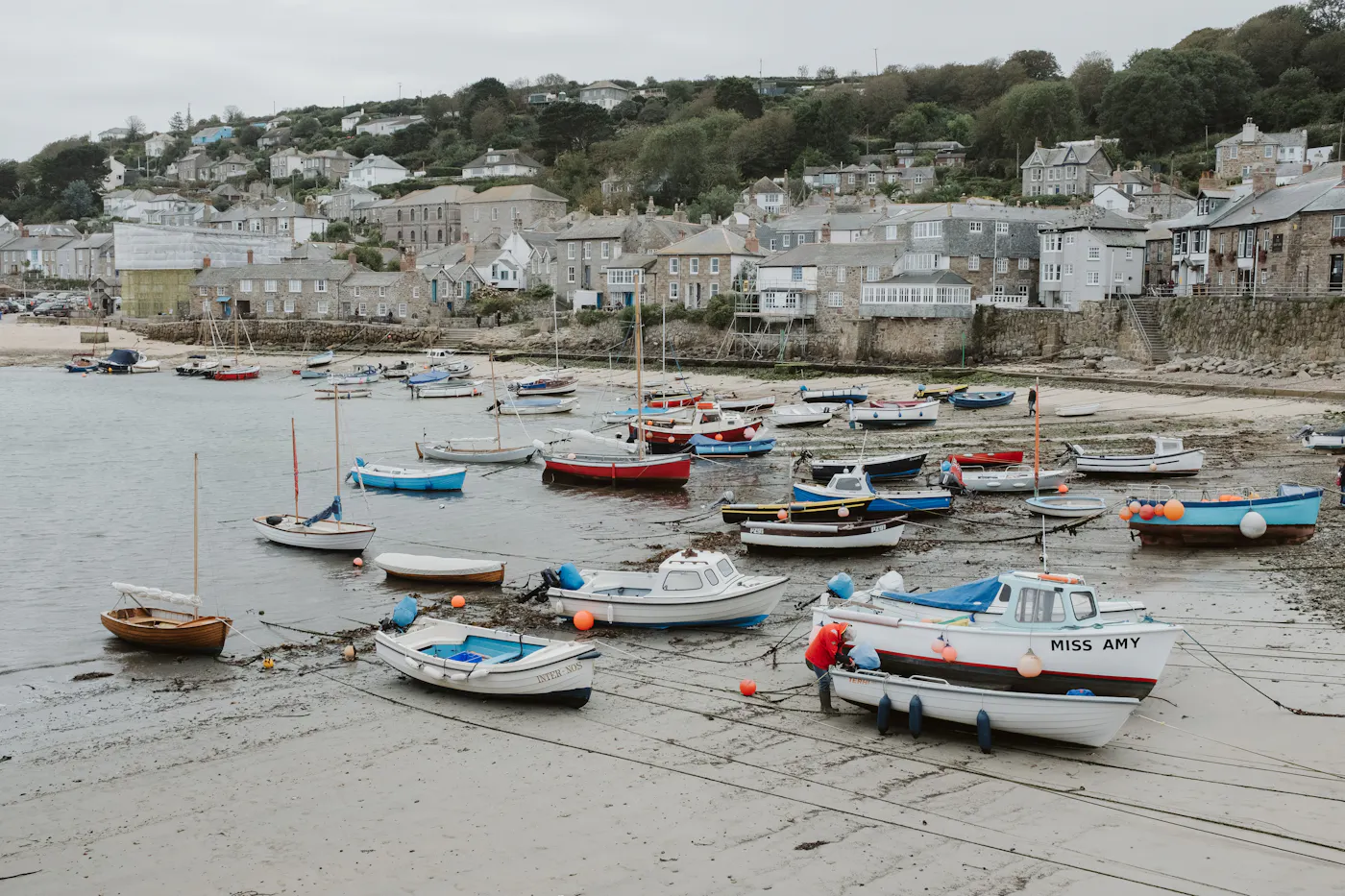 Small fishing boats resting on the sand of a Cornish harbour at low tide, with the village behind